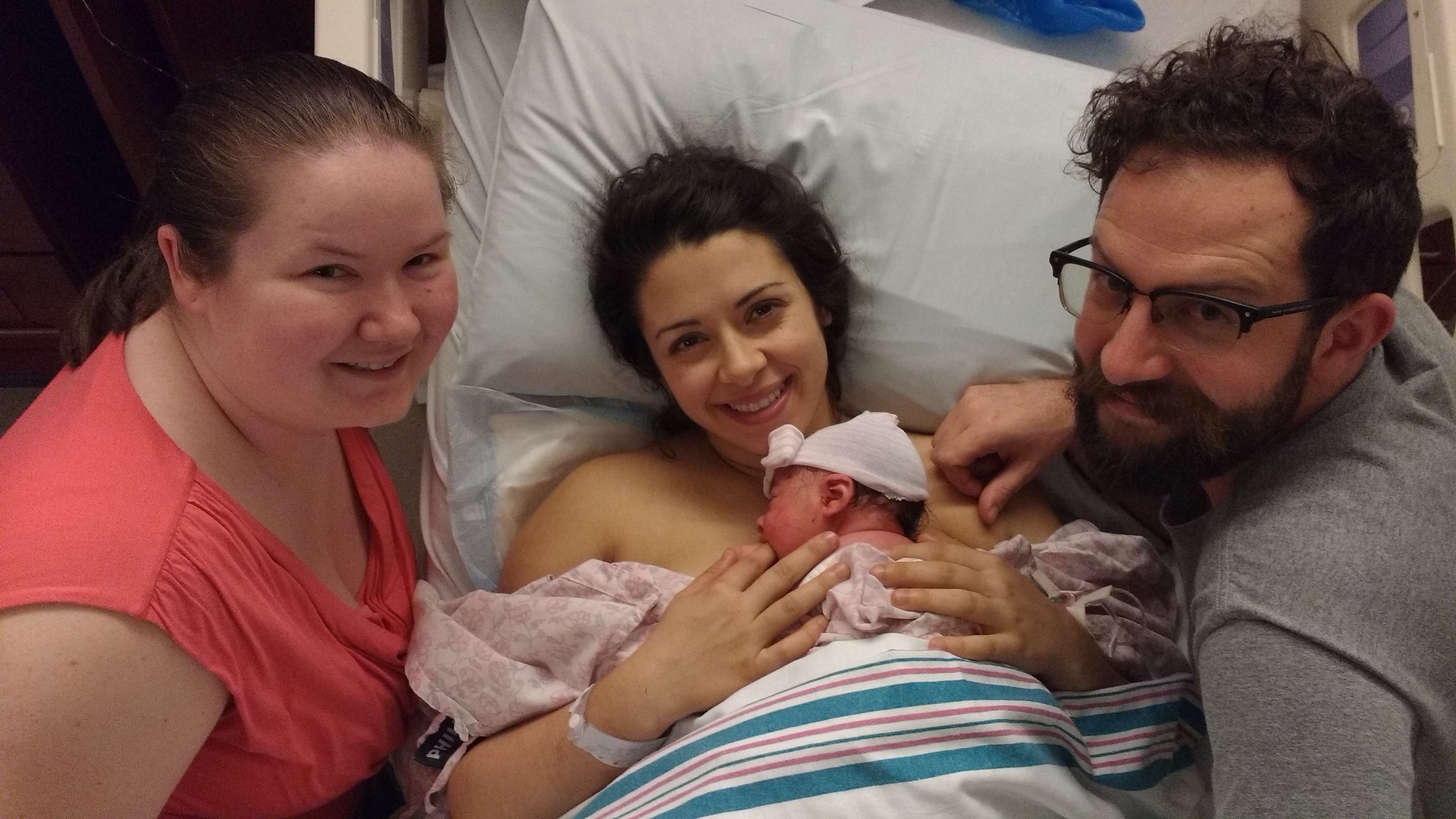 Doula, mother, baby, and father smiling at the camera