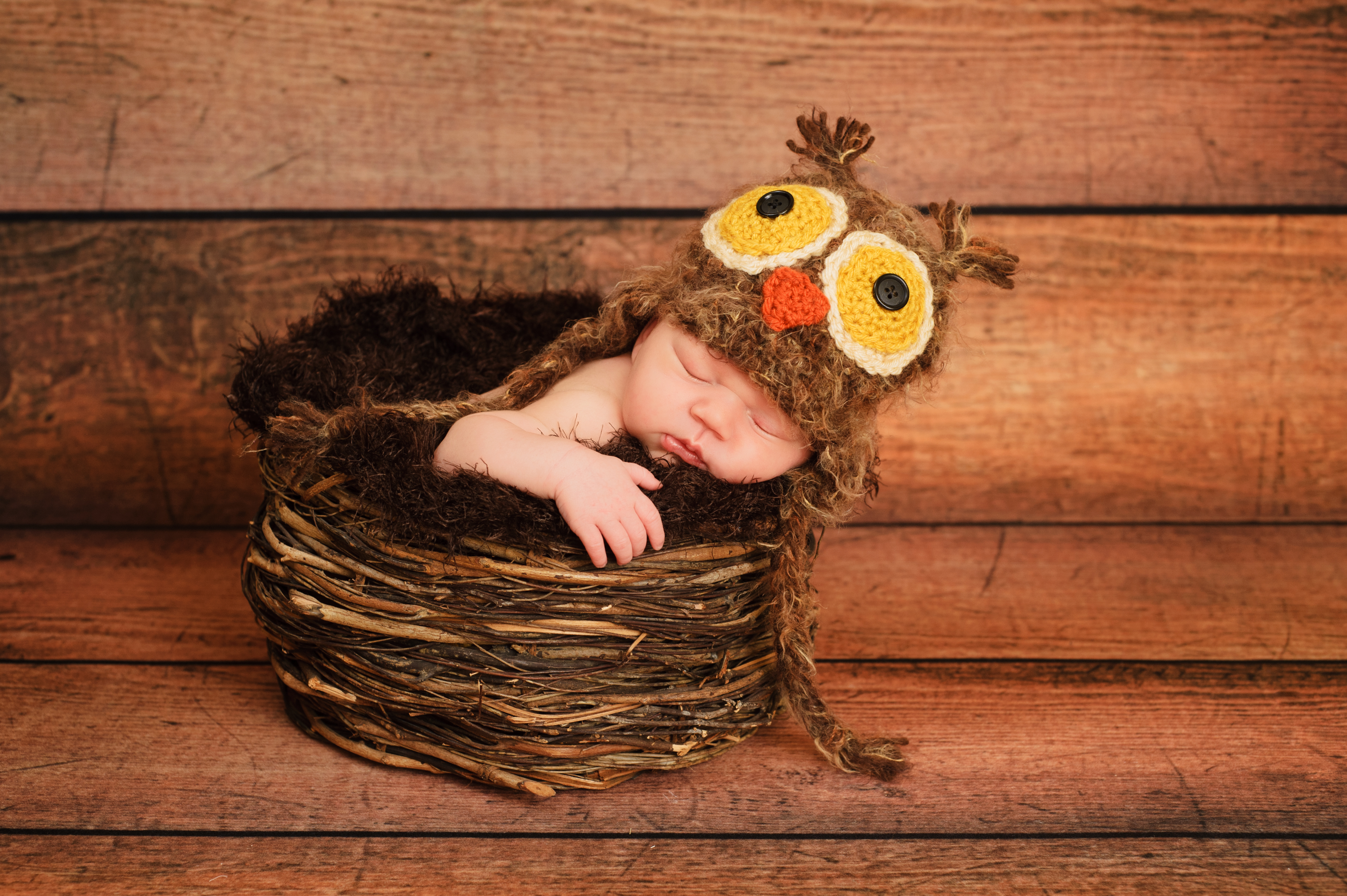 Baby laying in basket with owl hat on