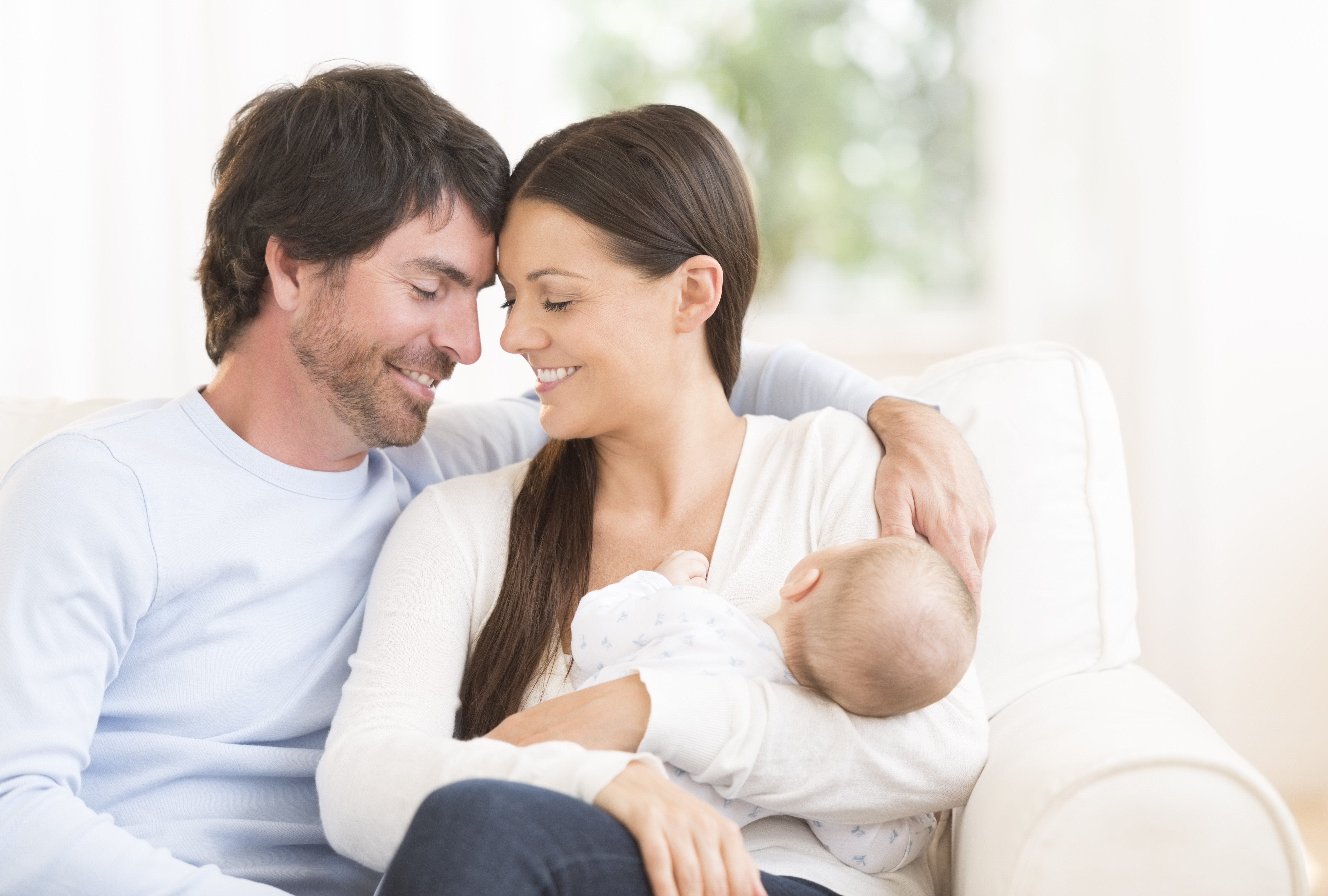 New parents holding baby on white couch