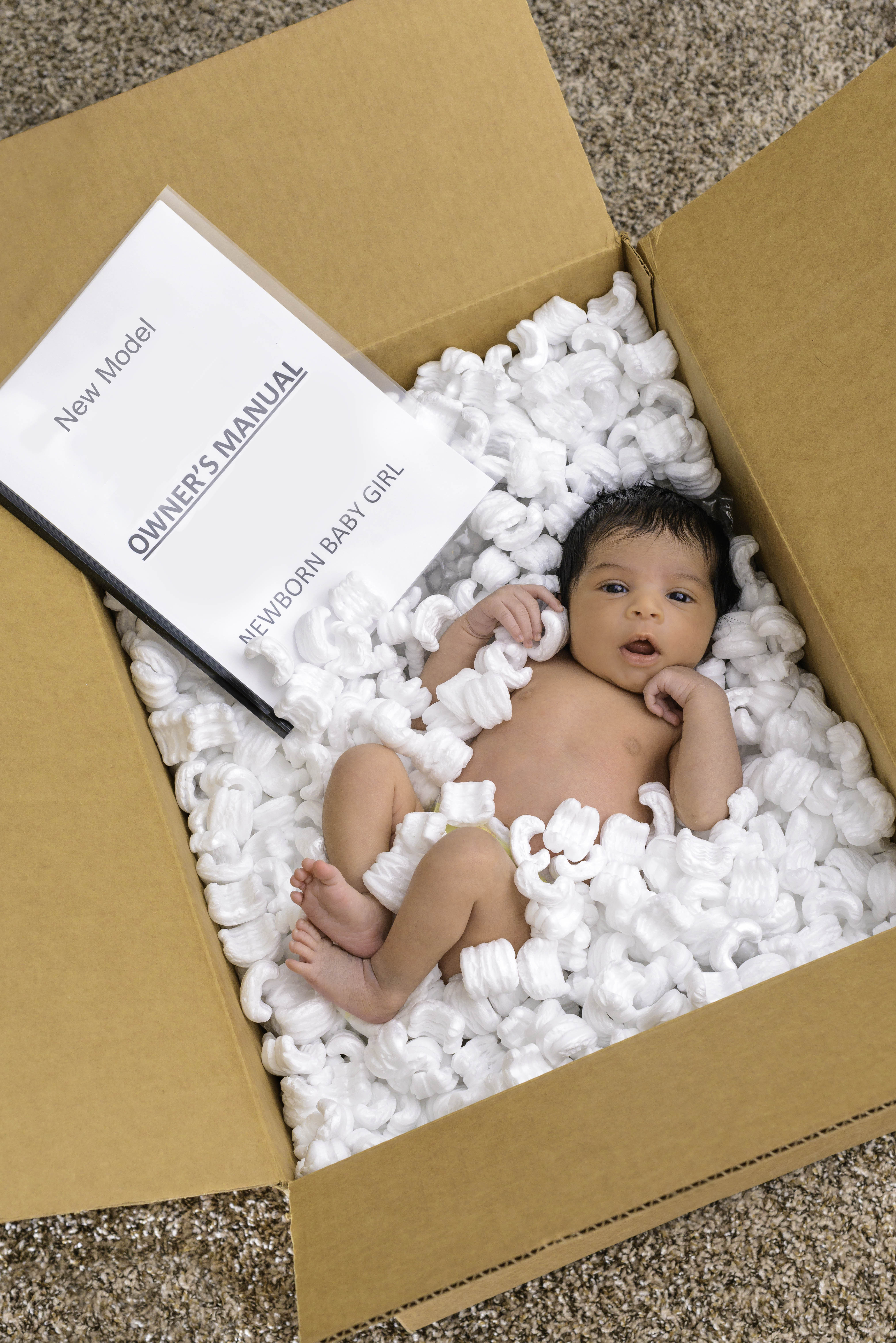 Baby in a box with packing peanuts and "Owner's Manual"